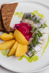 Elegant arrangement of herring fillets paired with rye bread, roasted potatoes, pickled onions, and green garnish on a white plate, culinary artistry. Restaurant or cafe menu, cookbook recipe