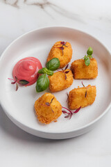 Deep-fried camembert cheese is served as an appetizer on a white plate, garnished with fresh basil leaves and a vibrant pink sauce. Restaurant or cafe menu, cookbook recipe