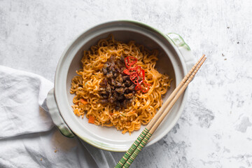 Overhead view of Spicy instant noodles with minced pork in a claypot, top view of spicy ramen noodles with pork in a donabe