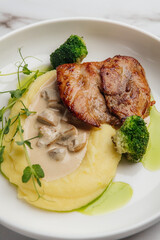 Grilled chicken breast is served with creamy mashed potatoes, steamed broccoli florets, fresh pea shoots, and a rich mushroom sauce. Restaurant or cafe menu, cookbook recipe