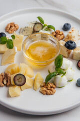 Round white plate with assorted cheese, honey, blueberries, walnuts and basil leaves, arranged in a beautiful composition, creating food presentation. Restaurant or cafe menu, cookbook recipe