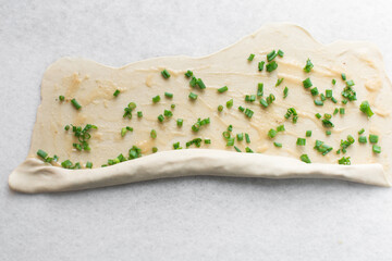 Overhead view of raw chinese scallion pancakes being rolled on white countertop, top view of homemade scallion pancakes, process of making cong you bing