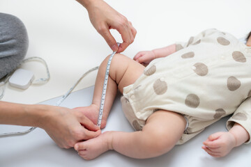 Mother measuring baby leg length with tape measure