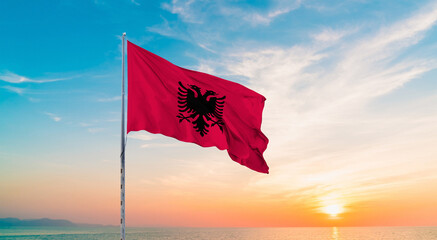 Waving flag of Albania against the background of a sunset or sunrise. Albania sky with flying flag beauty.  Concept of national holidays. Albania flag for Independence , Commemoration Day.