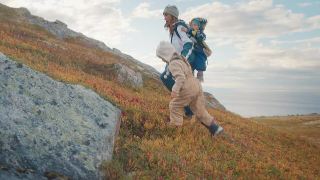 Mother hiking on a mountain with two children, one on her back and one holding her hand. Russia, Teriberka