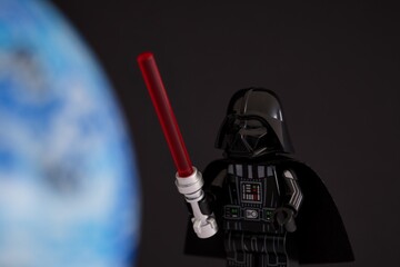 Naklejka premium Tambov, Russian Federation - November 14, 2024 Lego Darth Vader minifigure with red lightsaber against a black background with blue planet