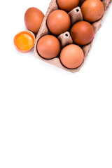 brown eggs in an egg tray, next to the tray there is a whole and a broken egg.