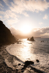 Waves crashing on the coast of Spain, in Basque Country. Steep cliffs drop down to the Bay of Biscay and sea stacks are present in the water. The setting sun casts golden light on the seascape.