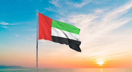 Waving flag of United Arab Emirates against the background of a sunset or sunrise. United Arab Emirates sky with flying flag beauty.  United Arab Emirates flag for Independence and Commemoration Day.