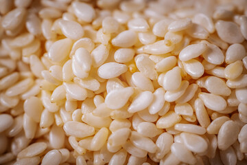 A macro shot of white sesame seeds showcasing their smooth texture and oval shape, commonly used in...