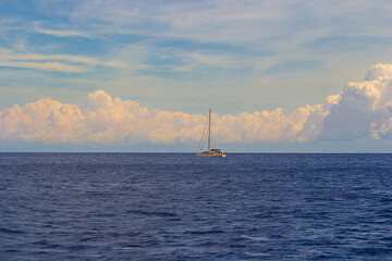Tranquil sailboat on serene sea under blue sky with fluffy clouds. Cumulus clouds over the sea in...