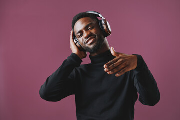 A stylish young man of African descent enjoys music with headphones, smiling confidently against a...