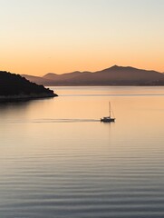 Serenity at Dawn:  A lone sailboat glides through tranquil waters under a serene sky painted with the soft hues of sunrise.  The distant mountains offer a majestic backdrop to this peaceful scene.