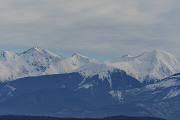 High snowy cold mountains peaks in winter over little clouds with rocky shapes