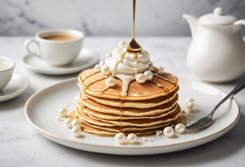 A stack of three golden-brown pancakes drizzled with white chocolate sauce, served with a dollop of whipped cream and topped with edible pearls