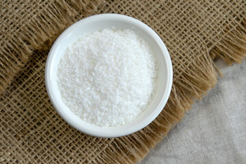 Coconut chips in white bowl on rough linen background. Top view, horizontal
