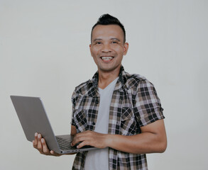 Asian man looking to the camera while holding a laptop and showing happy expression isolated on white background.