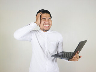 handsome asian man in white shirt holding laptop and showing dizzy, frustrated, depressed gesture while holding head