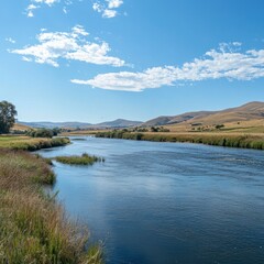 Serene river flowing through a picturesque valley under a blue sky with fluffy clouds.