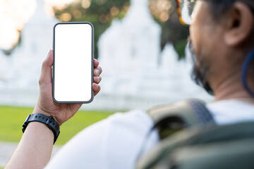 Smartphone mockup, man holding mobile phone with blank white screen outside at seaside landscape in...