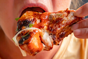 Enjoying a delicious grilled chicken wing with sauce during a casual summer gathering outside