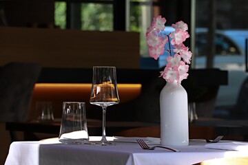 A table in a cafe set with glasses and a vase with a flower