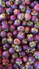 A close-up photo of a pile of fresh, ripe mangosteens, showcasing their vibrant purple color and unique texture.