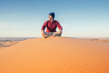 A handsome middle-aged man smiles happily posing with the sahara desert in the background. It is a sunny day and the sun is warm and bright. Travel, adventure and happiness concept