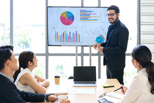 Businessman Giving Presentation Report to Business Team in the Conference Room, Shows Digital Information Graphics, Pie Charts about Company Growth on TV.