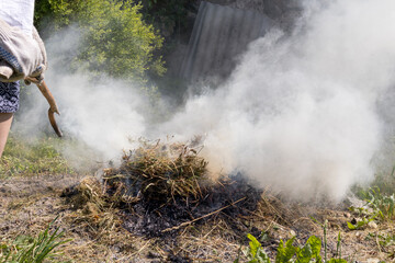 
A man lighting a smoky fire with a tree branch.