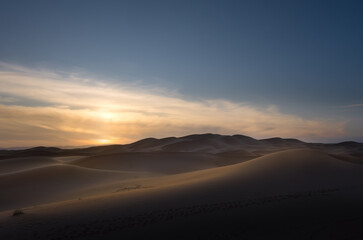 Beautiful panorama of a group of dunes at winter sunset in the Sahara Desert. There are some clouds left over from a storm and the sun is setting producing soft changes of light on the sand