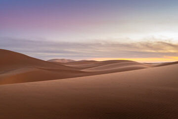 Beautiful and inspiring landscape of the Sahara desert in Morocco. The evening sun gently illuminates the sand of the dunes and the sky has incredible and magical clouds and pastel colors.