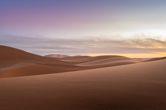 Beautiful and inspiring landscape of the Sahara desert in Morocco. The evening sun gently illuminates the sand of the dunes and the sky has incredible and magical clouds and pastel colors.