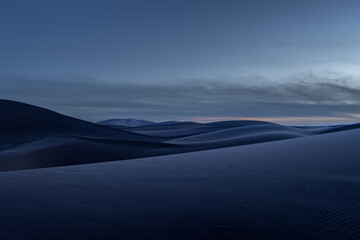 Stunning night panorama of the dunes of the Sahara desert in Morocco. The moonlight gently illuminates the dunes. It has just gotten dark and the sky still has some sunlight and clouds