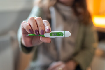 Woman showing a thermometer with thirty-nine degrees of fever, flu symptoms.
