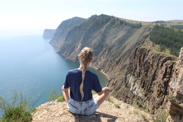 Naklejka premium girl sitting on a cliff with a breathtaking view during a hike to the mountains on an island in a lake