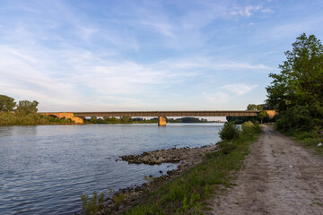 A wide view of a bridge spanning across a calm river, surrounded by lush green vegetation on both sides. 