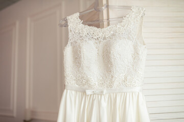 Chic white dress in soft light. A delicate white dress hangs in a softly lit room, showcasing intricate lace and a flowing skirt design.