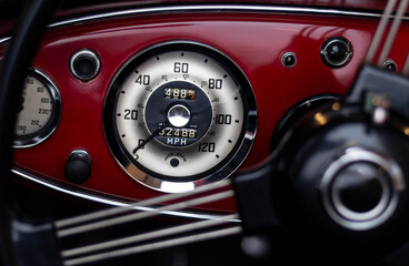 Detailed close-up of a classic car's speedometer and dashboard, featuring a retro design with chrome accents and deep red paneling. Timeless automotive elegance.