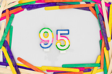 Number 95 shape birthday candles in a colorful popsicle sticks frame border on white background