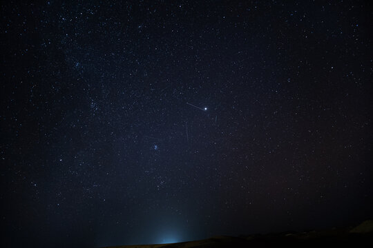 Celestial panorama of the stars over the dunes of the Sahara desert. You can see the stars shining and several shooting stars with their trail in the sky. They are the Geminids of December