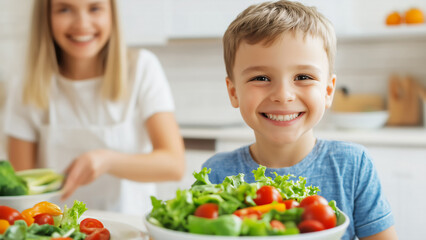 Lachender Junge steht in der K&uuml;che vor einer Sch&uuml;ssel mit frischem, gesundem Salat, im unscharfen Hintergrund seine l&auml;chelnde Mutter, Gesunde Ern&auml;hrung f&uuml;r Kinder und Familie