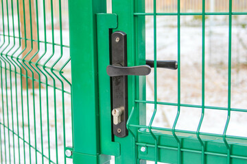 Green gate with secure lock mechanism in an outdoor setting during daylight