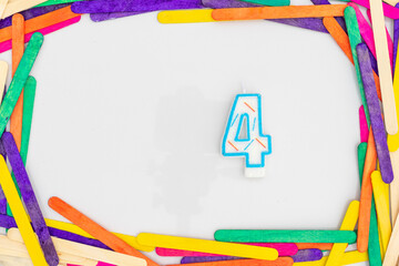 Four numerical number shape rainbow colors candle in a colorful wooden sticks frame border on white...