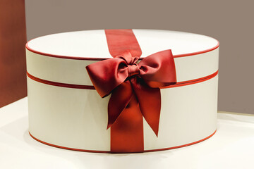 Beautiful elegant oval white gift box tied with red ribbon with a bow.