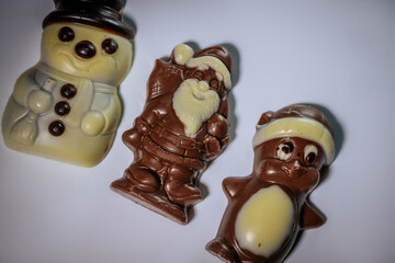 Close-up of three Christmas themed chocolates shaped like a snowman, Santa Claus and a penguin made of milk and white chocolate and placed on a white background. Perfect for holiday and festive themes