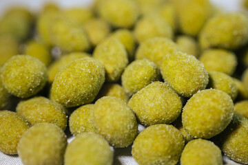 A close-up view of bright yellow-green wasabi-flavored nuts coated in a fine powder, creating a spicy and crunchy snack. Blurred background for emphasis.