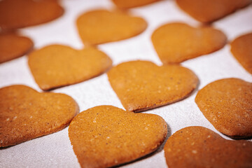 Rows of heart-shaped golden brown gingerbread cookies are arranged on a white surface. Their warm tones and rustic texture evoke love and coziness.