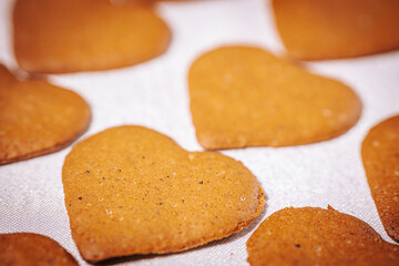 Rows of heart-shaped golden brown gingerbread cookies are arranged on a white surface. Their warm tones and rustic texture evoke love and coziness.