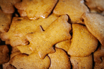A close-up view of a pile of golden brown gingerbread cookies in various festive shapes, including bells and stars. Their rustic texture creates a cozy, homemade feel.